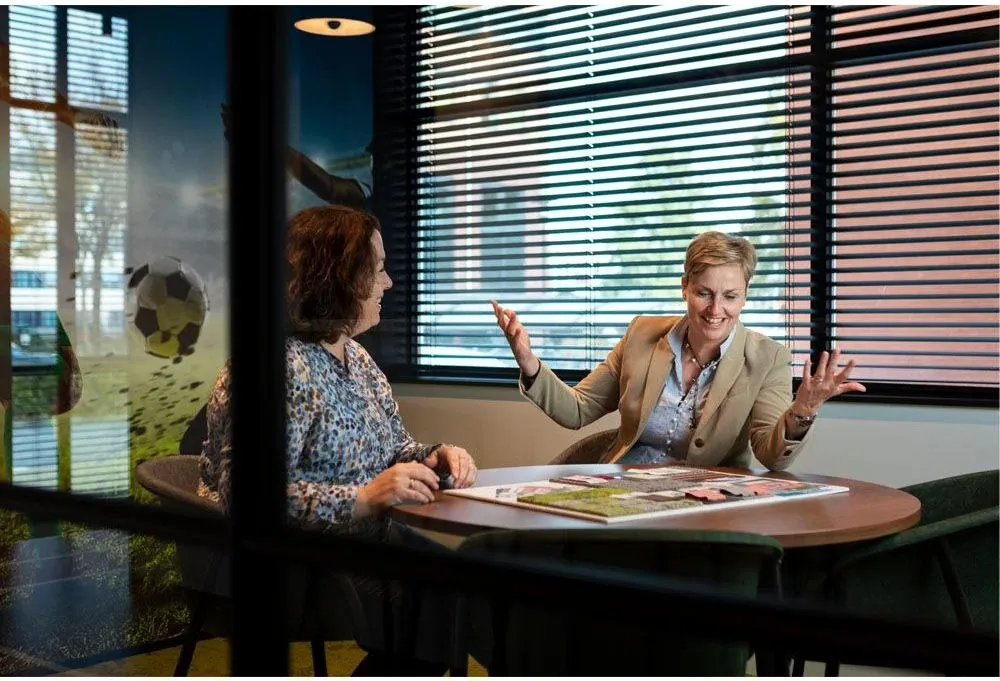 Twee vrouwen in overleg aan een vergadertafel met drukwerk